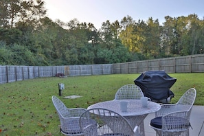 Une terrasse extérieure avec une table ronde et quatre chaises, un barbecue et une clôture en bois en arrière-plan.