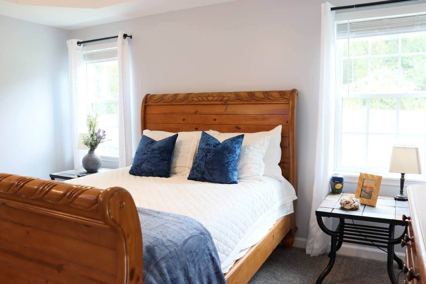 Un dormitorio con una cama de madera, ropa de cama blanca y una mesita de noche con una lámpara.