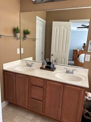 A bathroom with two sinks, wooden cabinets, a large mirror, and a door leading to another room.