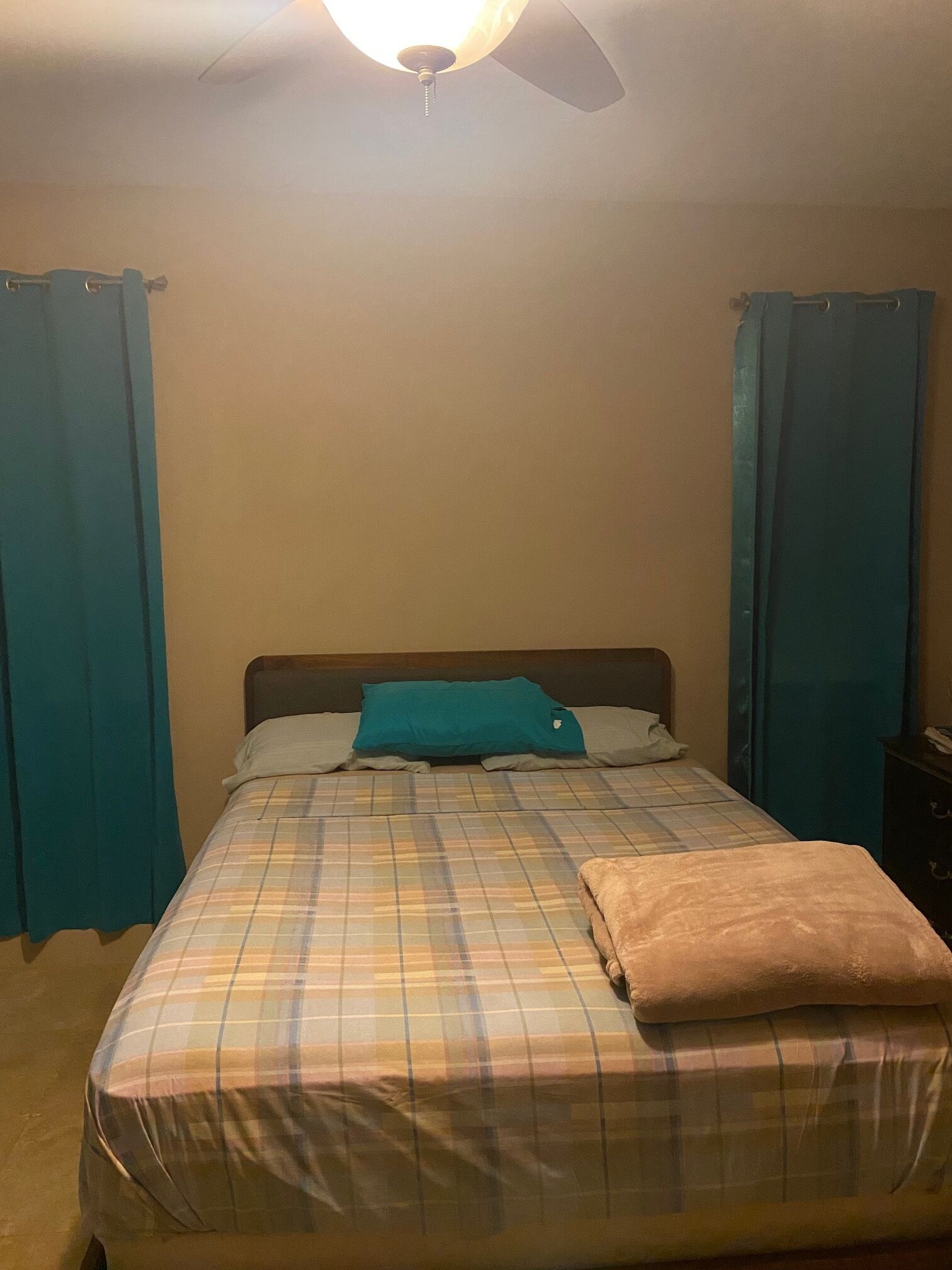 A bed with a plaid bedspread, a teal pillow, and a brown throw blanket.