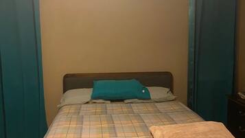 A bed with a plaid bedspread, a teal pillow, and a brown throw blanket.