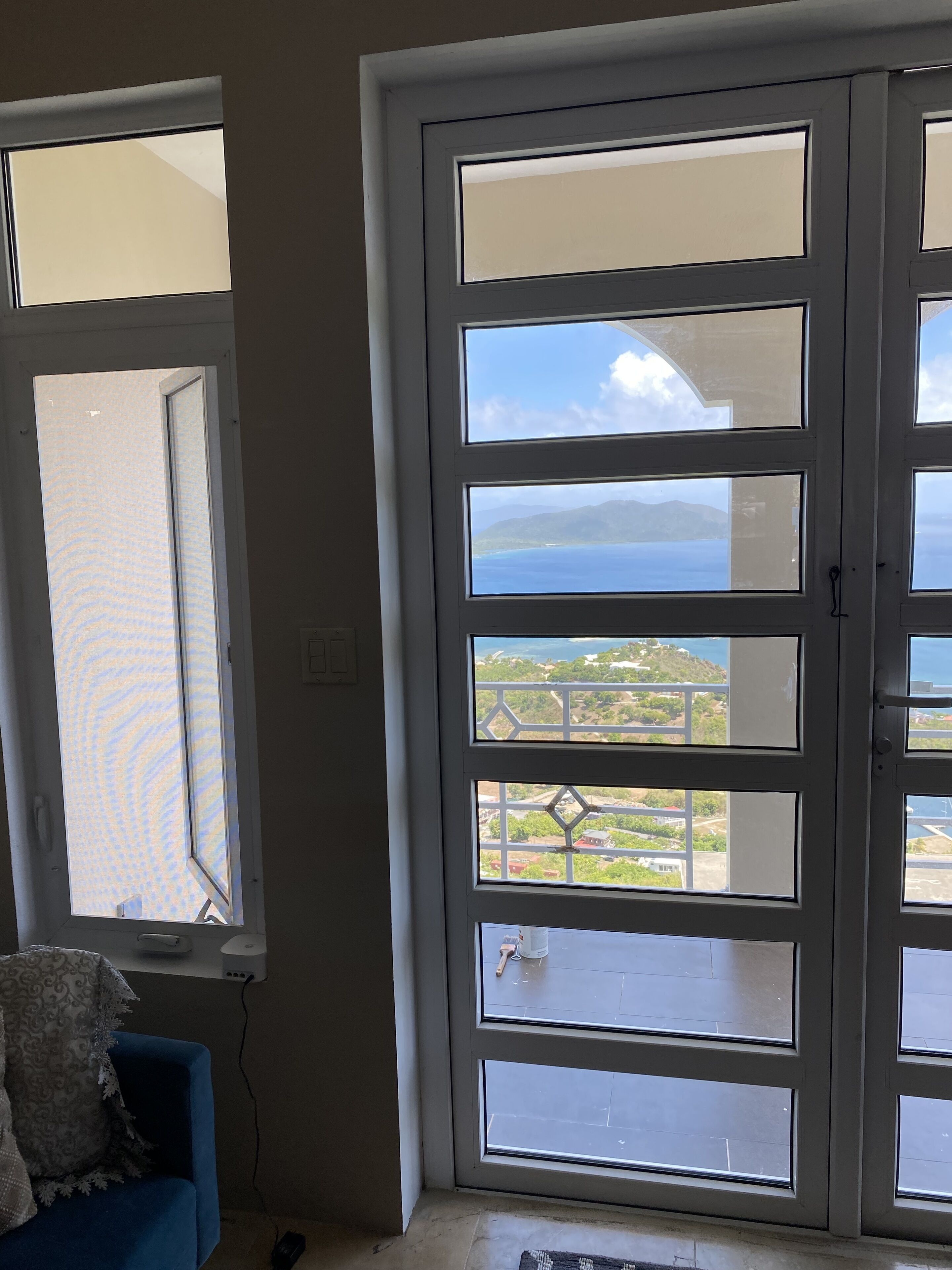 Una habitación con un gran ventanal corredera que da a un balcón con vistas al mar y al follaje.