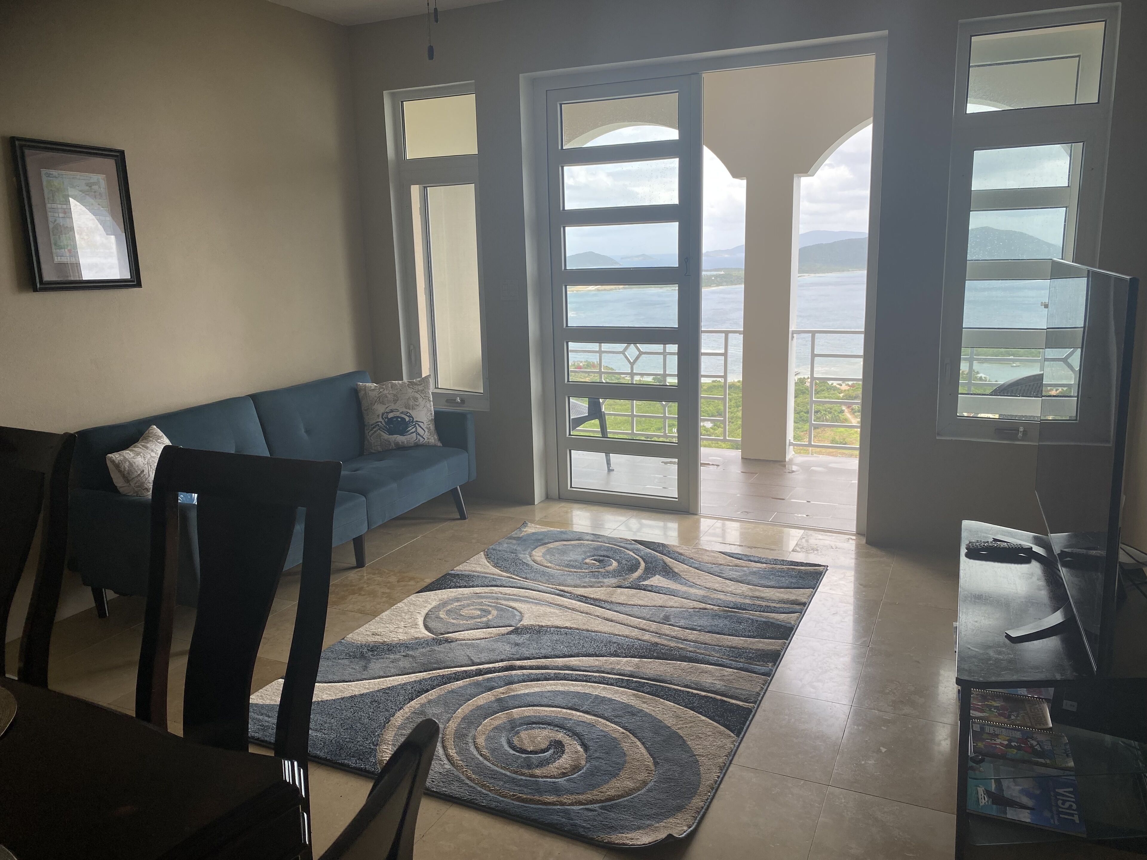 Un soggiorno con un divano blu, un tappeto decorato e vista mare attraverso ampie finestre.