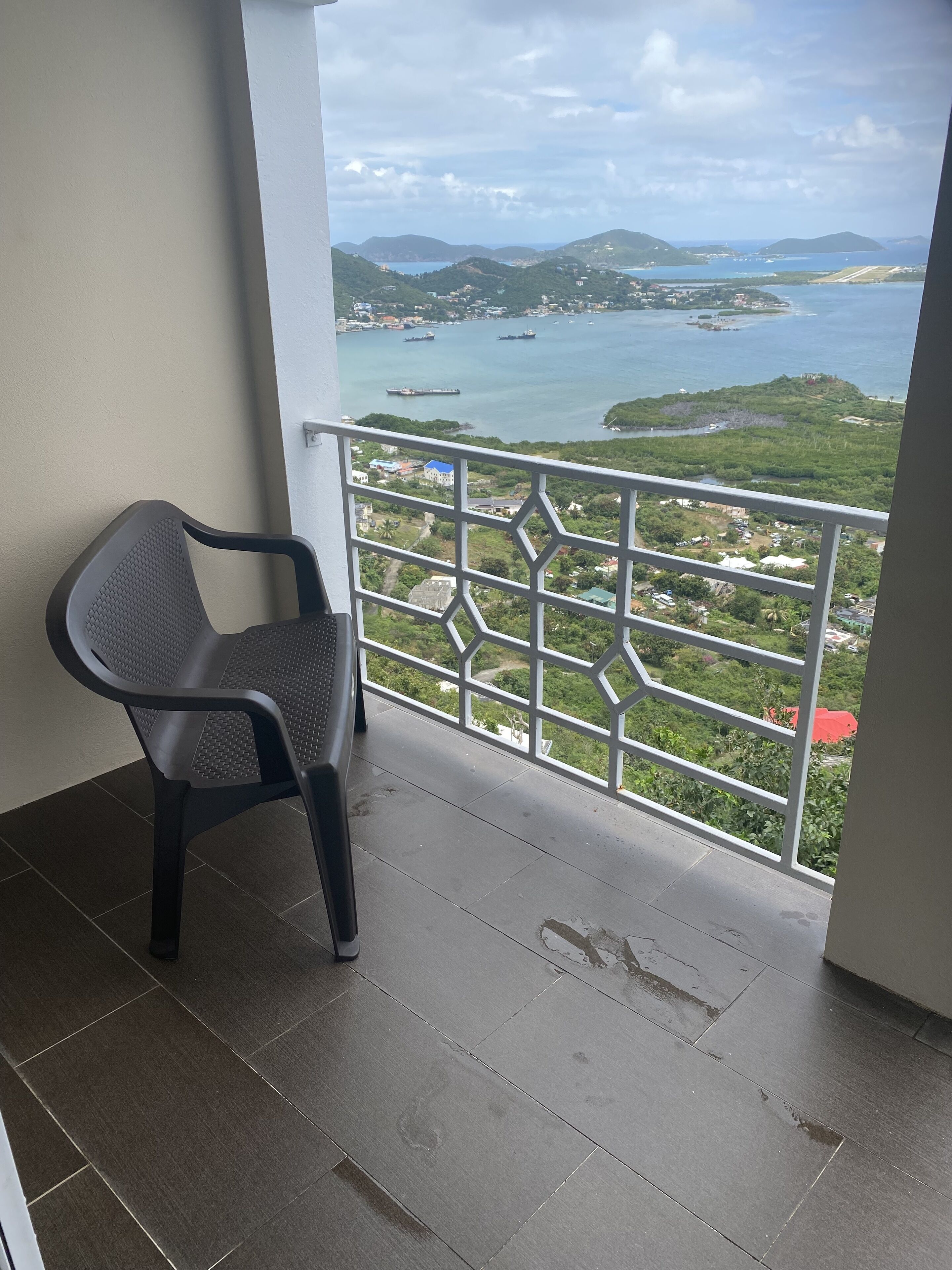 A balcony with a view of a coastal landscape, including hills and a body of water.