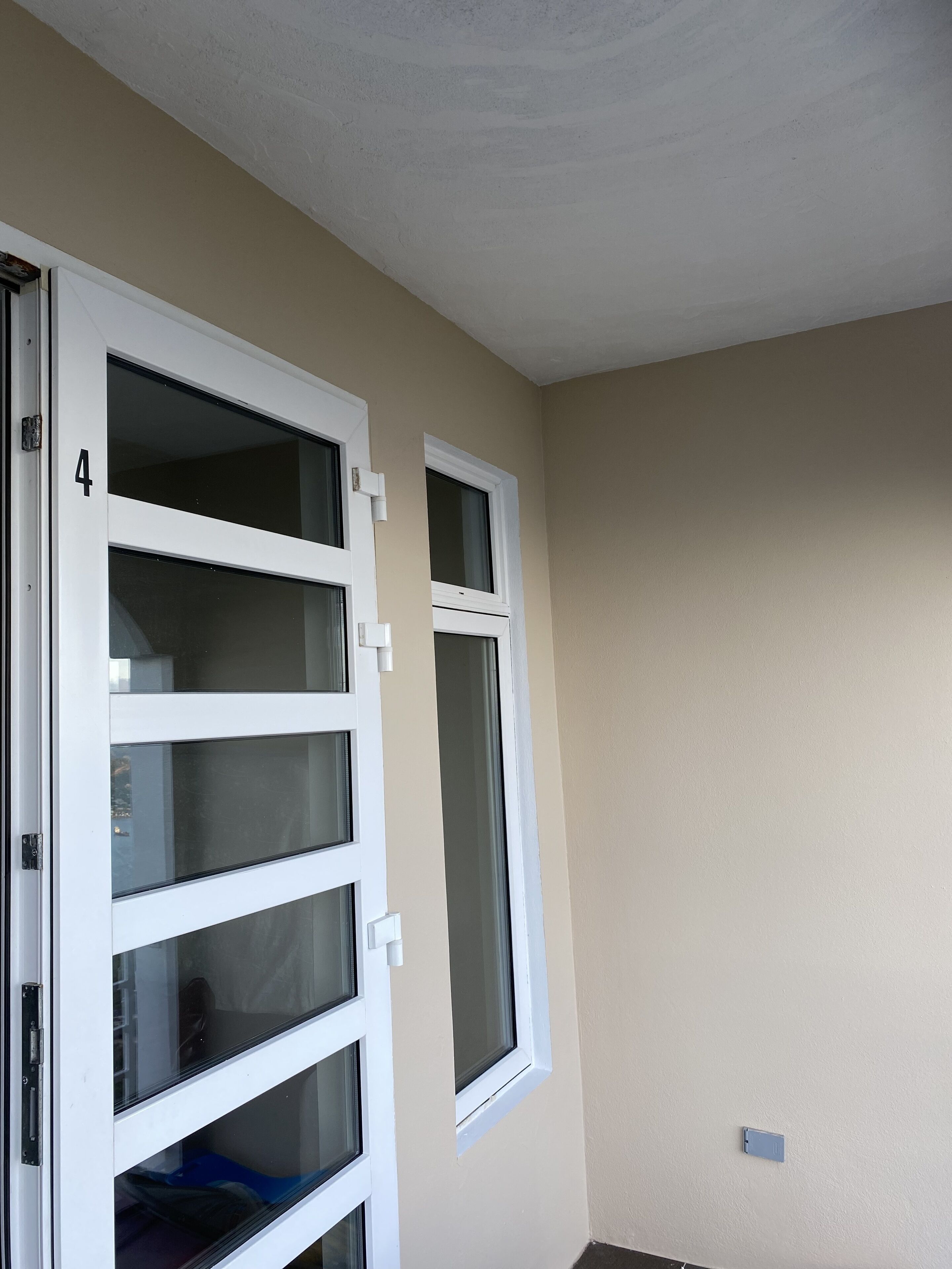 Ein Zimmer mit einer beigen Wand, einer weißen Tür mit Glasfeldern und einem Fenster.