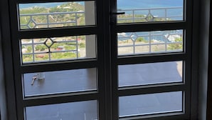 Une porte dotée de plusieurs panneaux de verre offrant une vue sur un paysage côtier, comprenant une étendue d’eau et des reliefs lointains.