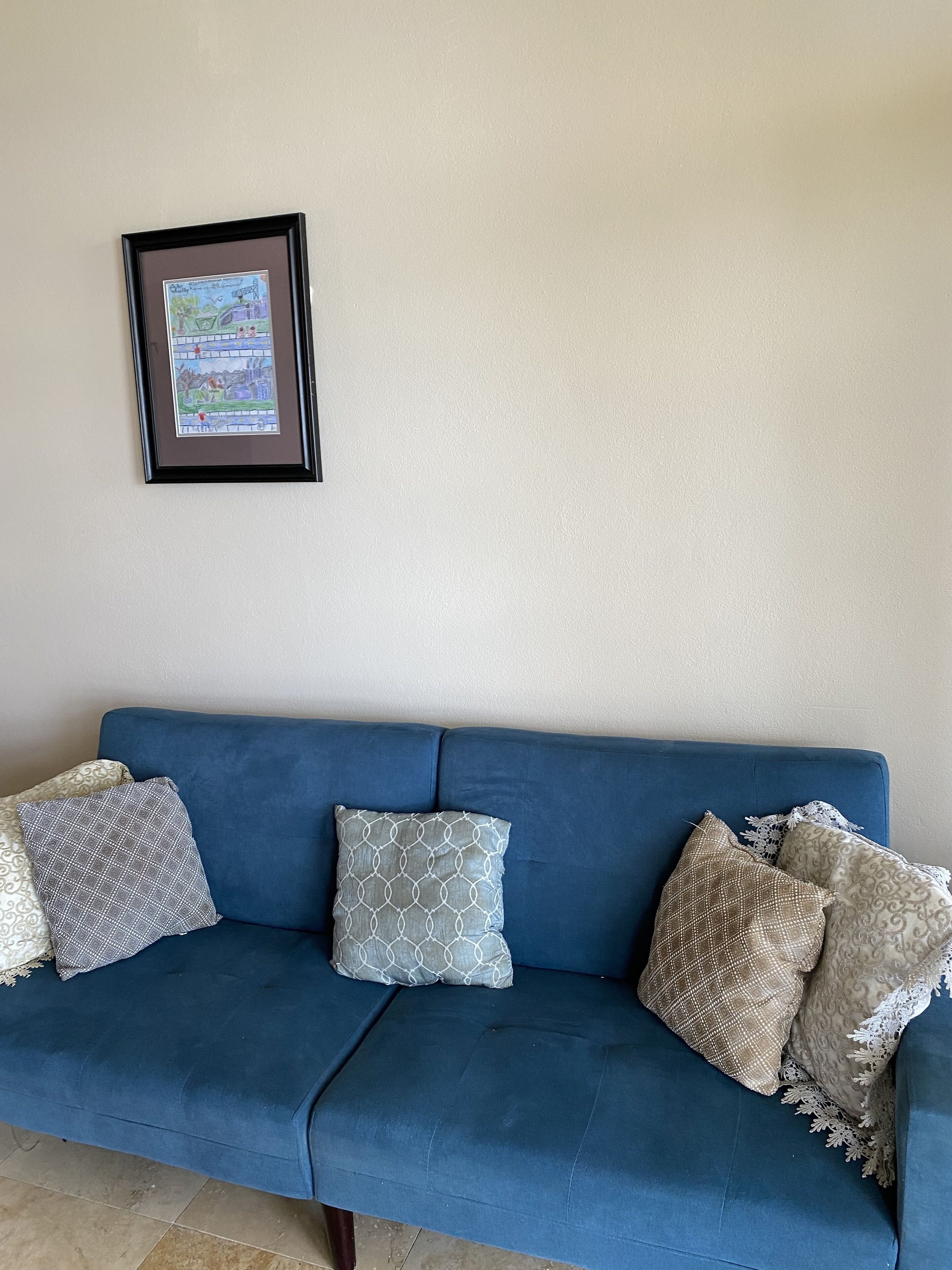 Un divano blu con cuscini a fantasia, su uno sfondo di parete neutra, con un quadro incorniciato sopra.
