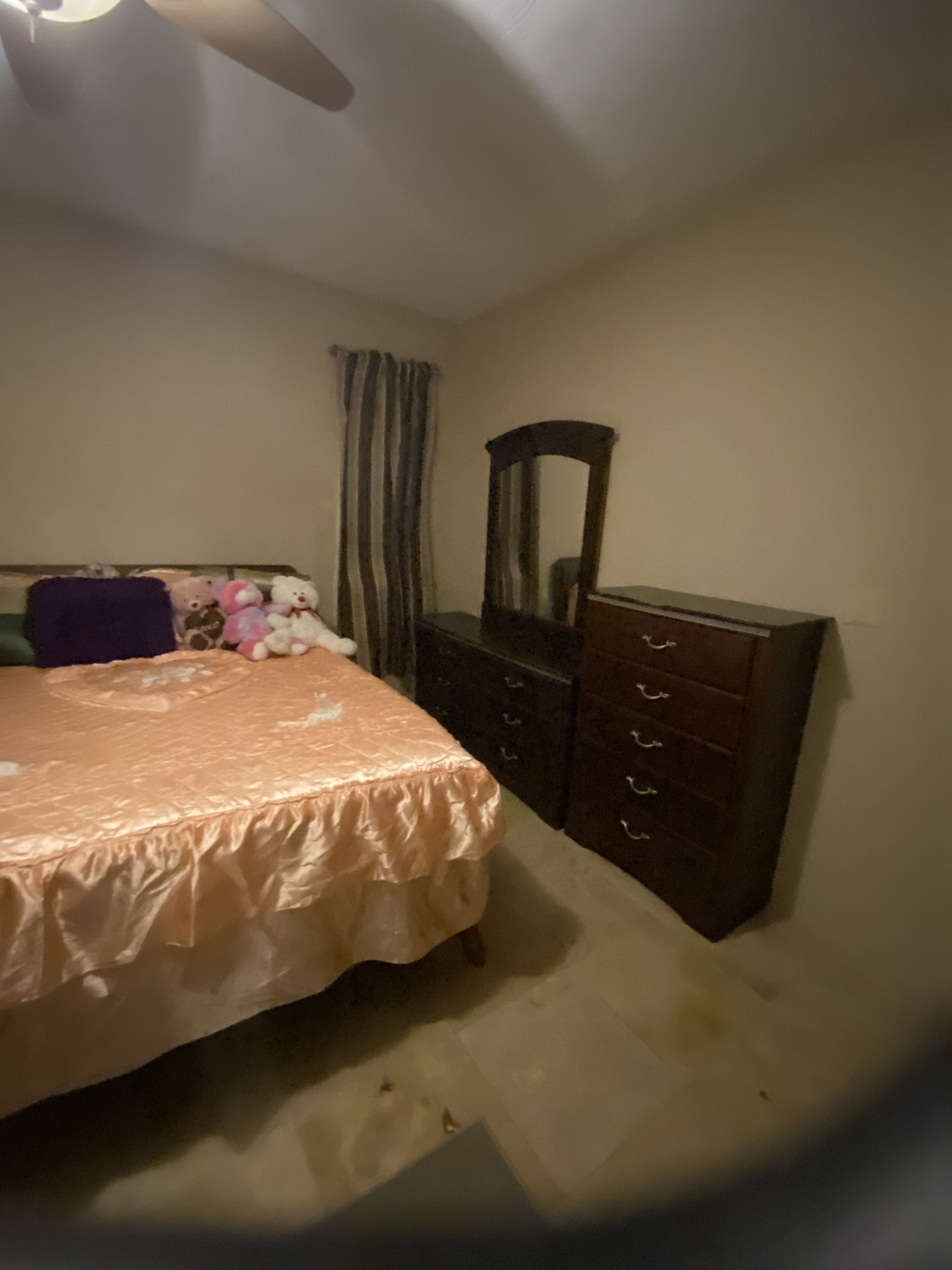 Ein Schlafzimmer mit Bett, Kommode, Spiegel und Vorhängen.