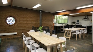 A spacious room with a large wooden table and white chairs, a brick wall with a circular window, and a kitchen area with modern appliances. - Tawonga Tourist Park (Tawonga)