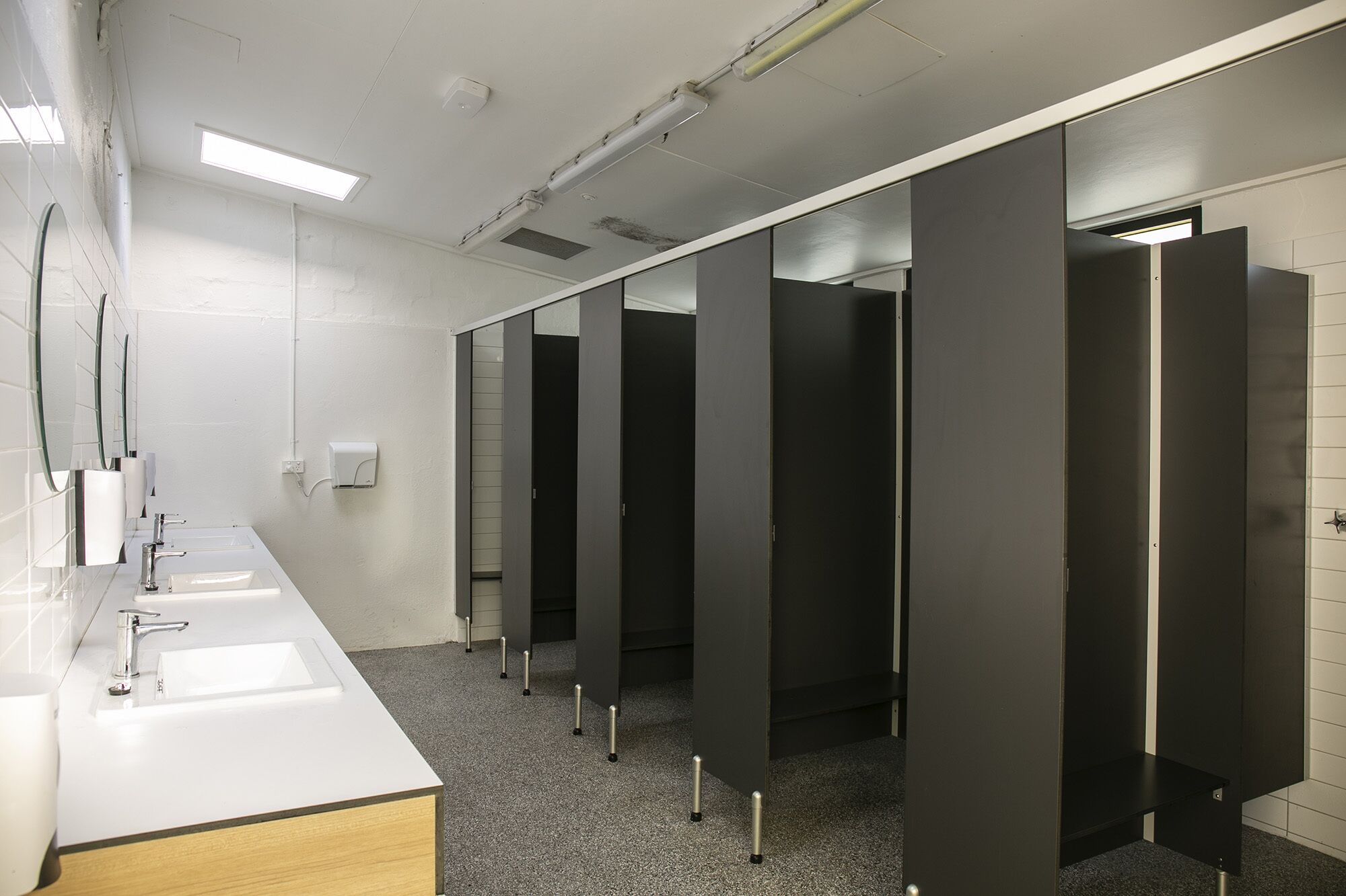 Un baño moderno con lavamanos blancos, espejos y cabinas oscuras.