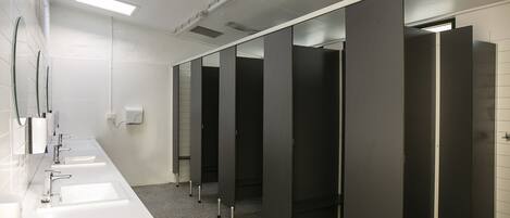 Un baño moderno con lavamanos blancos, espejos y cabinas oscuras.
