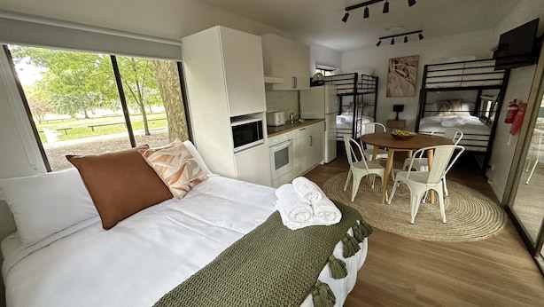 A compact hotel room with a bed, a kitchenette, a dining area, and a bunk bed. - Tawonga Tourist Park (Tawonga)