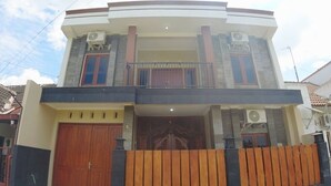 A two-story house with a balcony, a wooden gate, and a large wooden door. - Eltanin Homestay by FH Stay (Depok)