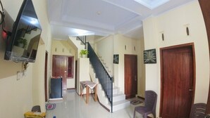 A spacious living area with a staircase, a flat-screen TV mounted on the wall, and a wooden door. - Eltanin Homestay by FH Stay (Depok)