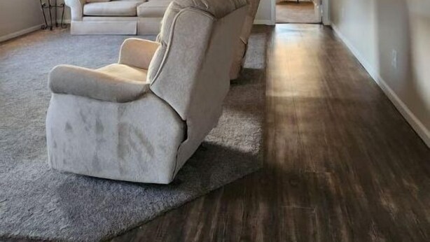 Un salon spacieux avec un grand canapé d’angle gris, un ventilateur de plafond et un plancher en bois.