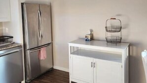 Une cuisine avec des meubles blancs, un réfrigérateur en acier inoxydable et un plan de travail blanc agrémenté d’un panier.