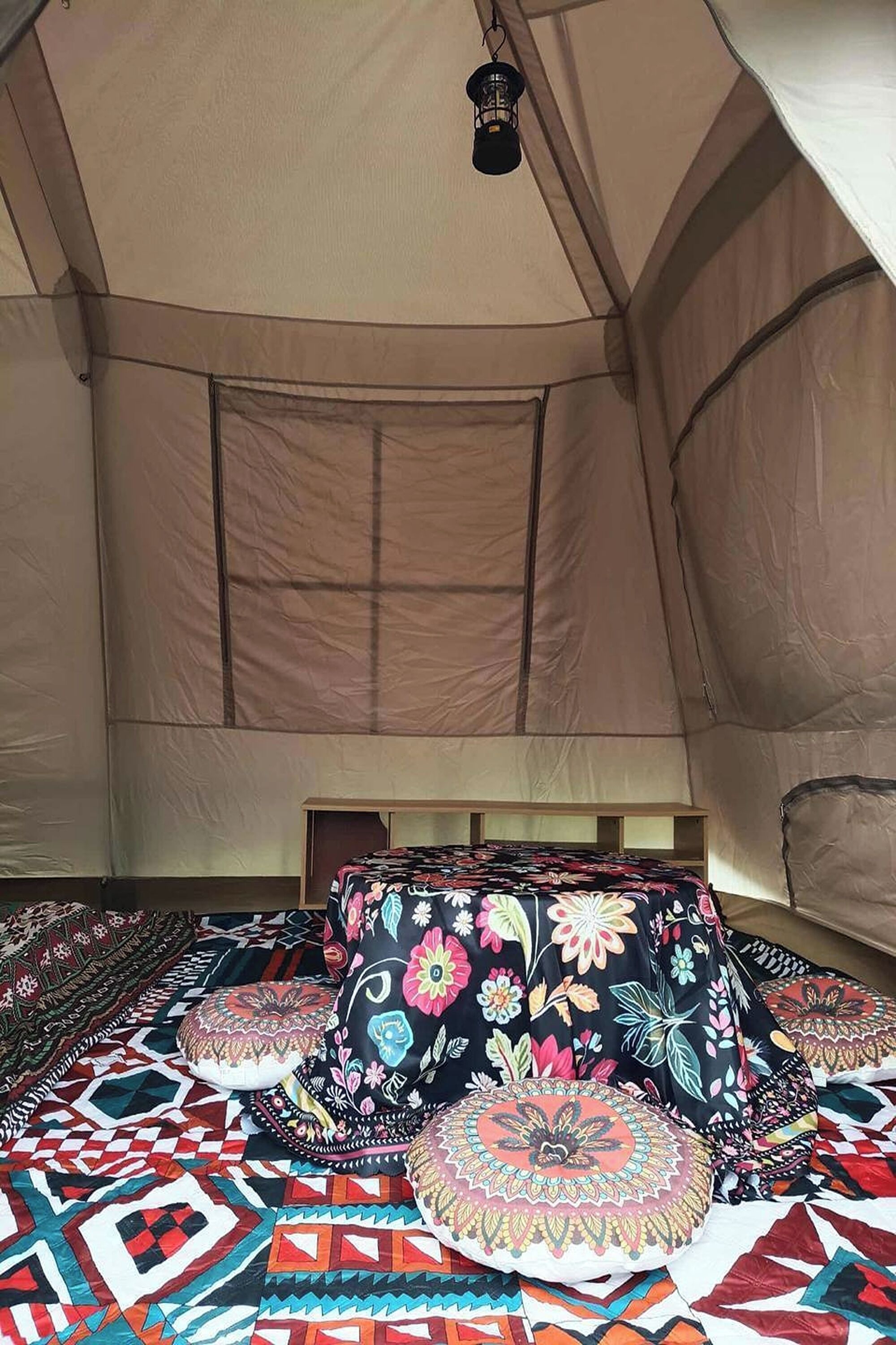 A tent interior with a bed, pillows, and a hanging light fixture.