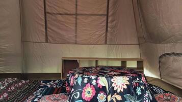 A tent interior with a bed, pillows, and a hanging light fixture.