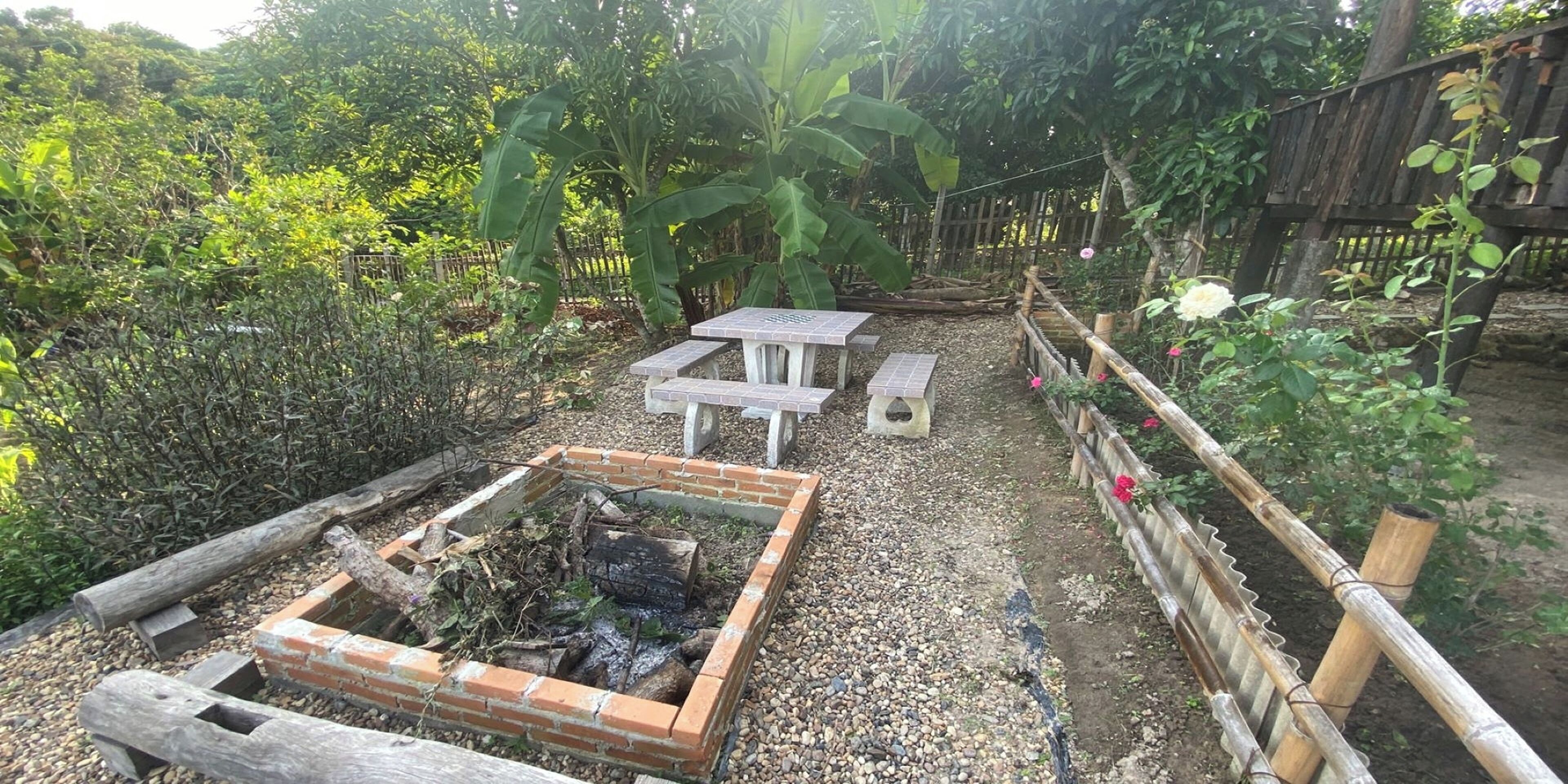 A garden with a brick fire pit, a wooden bench, and a table.