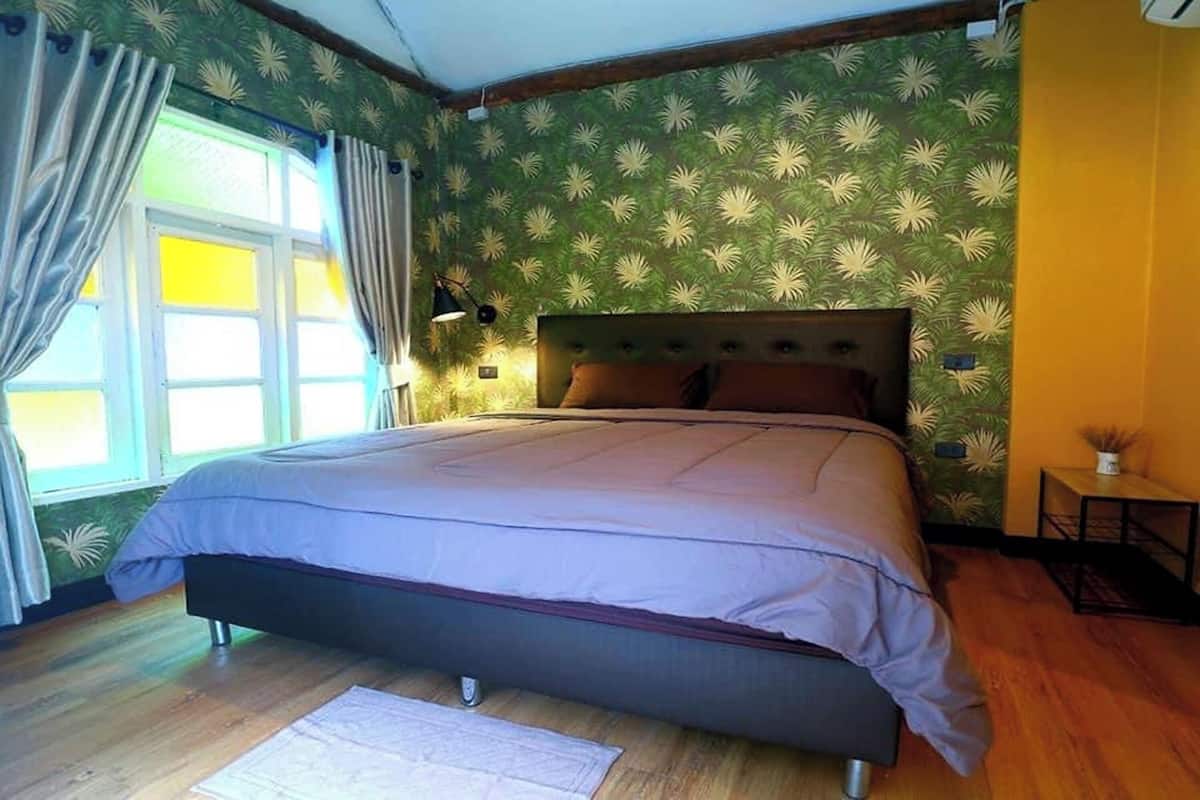 A bedroom with a bed, curtains, a window, and a wall with a leafy pattern.