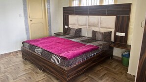 A bedroom with a wooden bed frame, a headboard with a padded section, and a window above the bed. - N V Villa Homestay (Kasauli)