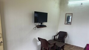 A room with a television mounted on the wall, a small table with two chairs, and a framed picture on the wall. - N V Villa Homestay (Kasauli)