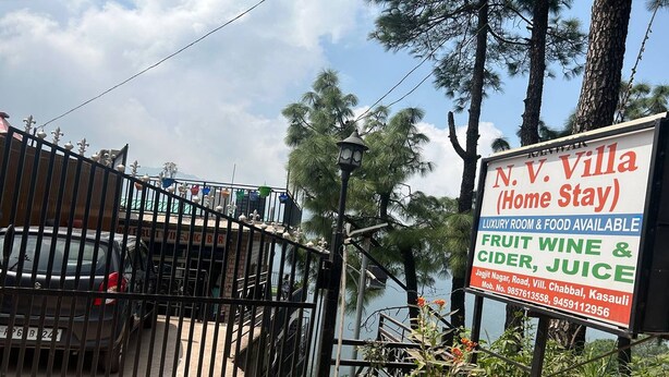 A sign for N.V. Villa (Home Stay) advertising luxury room and food availability, fruit wine & cider, juice, and contact information. - N V Villa Homestay (Kasauli)