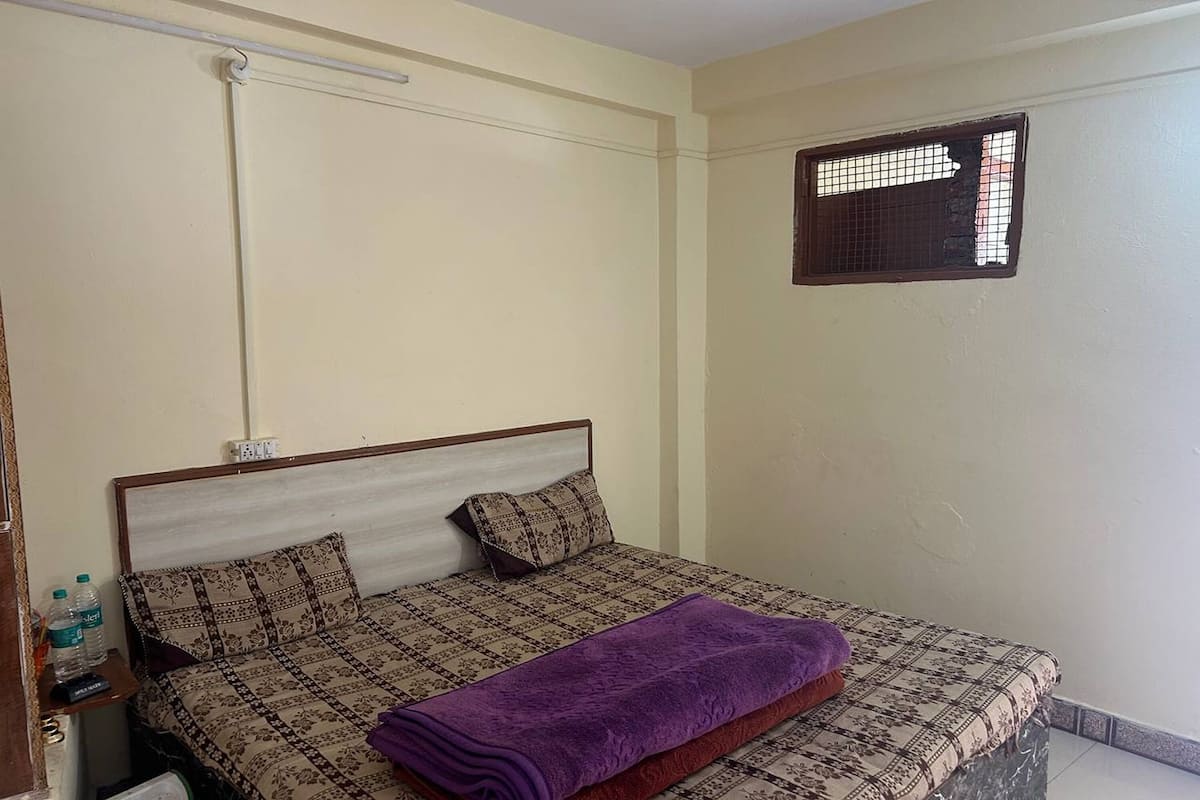 A single bed with patterned bedding, a purple blanket, and a headboard.