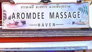 Ein Massage-Salon namens Aromdee Massage Haven mit Schilder, Eingang und Topfpflanzen.