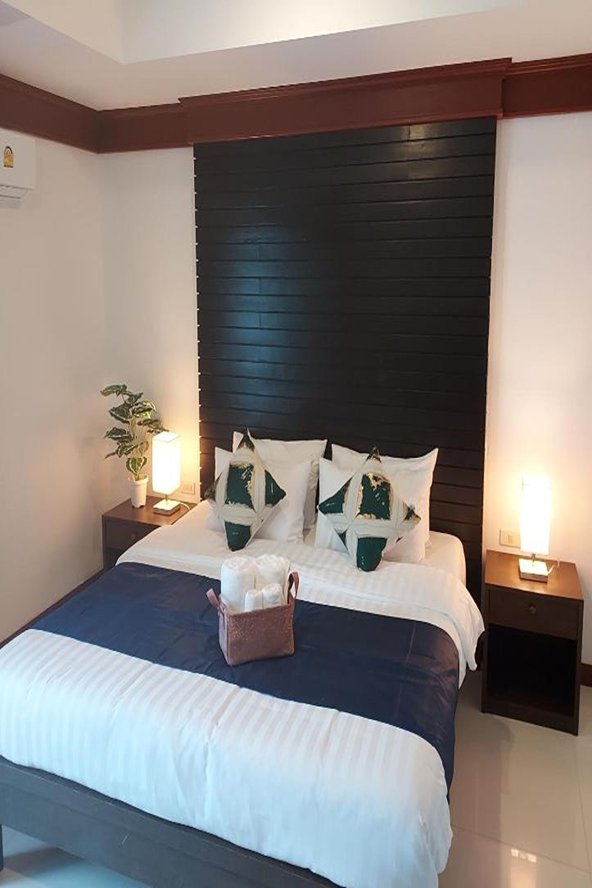 Een net opgemaakt bed met wit- en blauwe beddengoed, twee bedlampen en een donker houten hoofdbord.