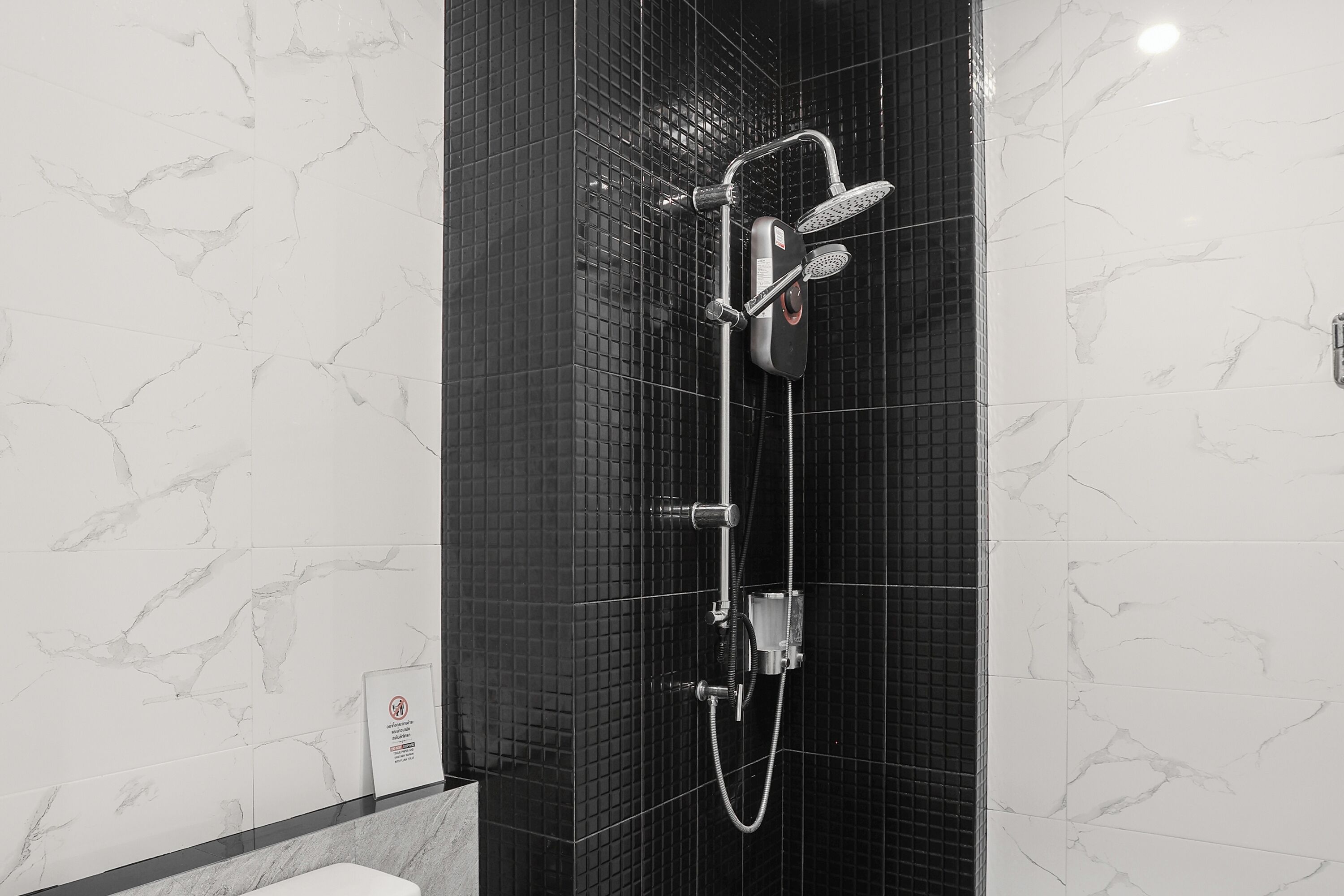 Une salle de bain moderne avec une douche à l’italienne aux carreaux noirs, un sèche-mains apparent et un mur carrelé arborant un motif évoquant le marbre.