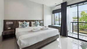 A modern hotel room with a large bed, a nightstand, a window with a view of greenery, and a balcony. - De Piraya Residence (Mai Khao)