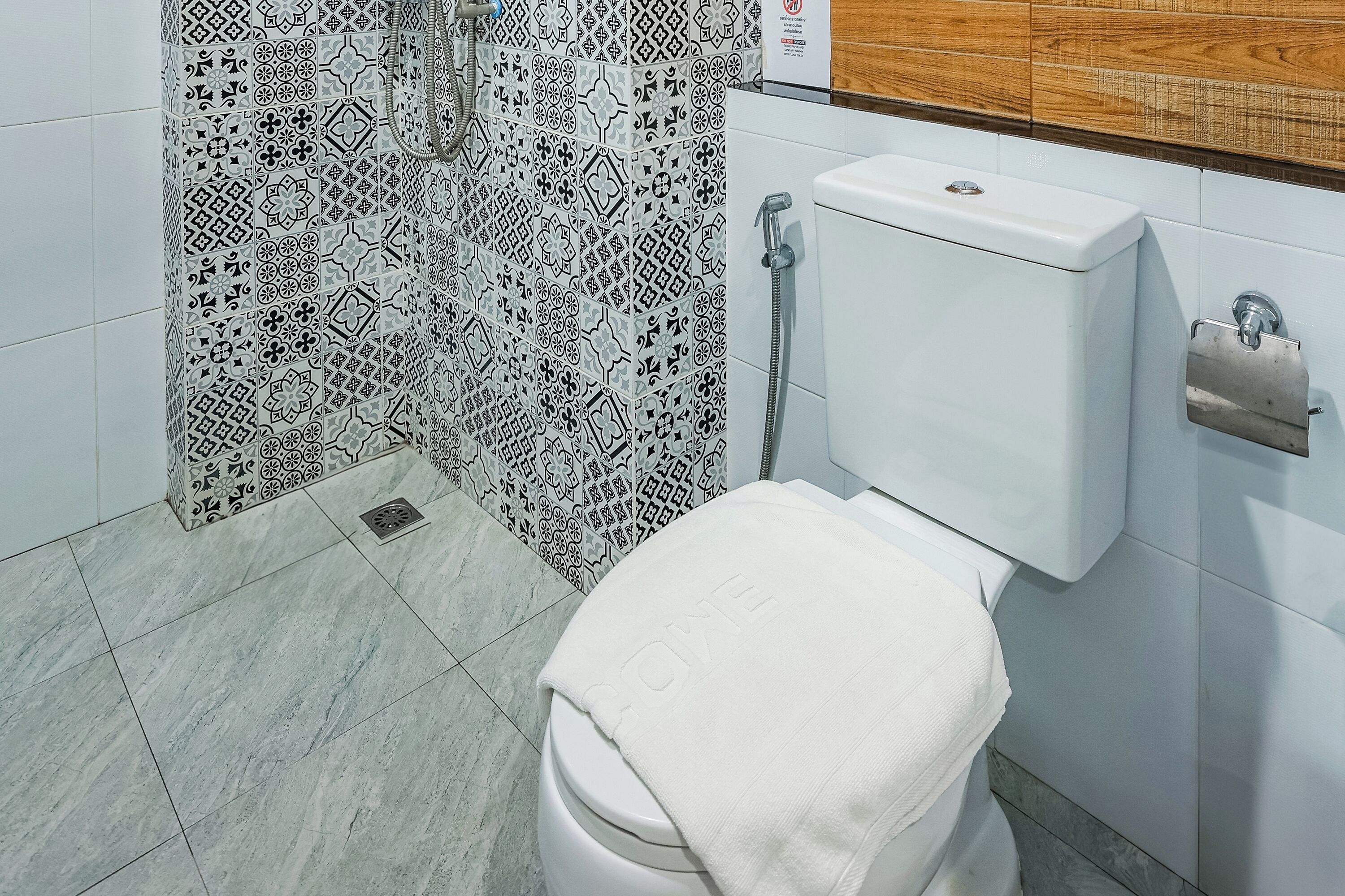 Casa de banho com sanita, chuveiro e azulejos estampados.