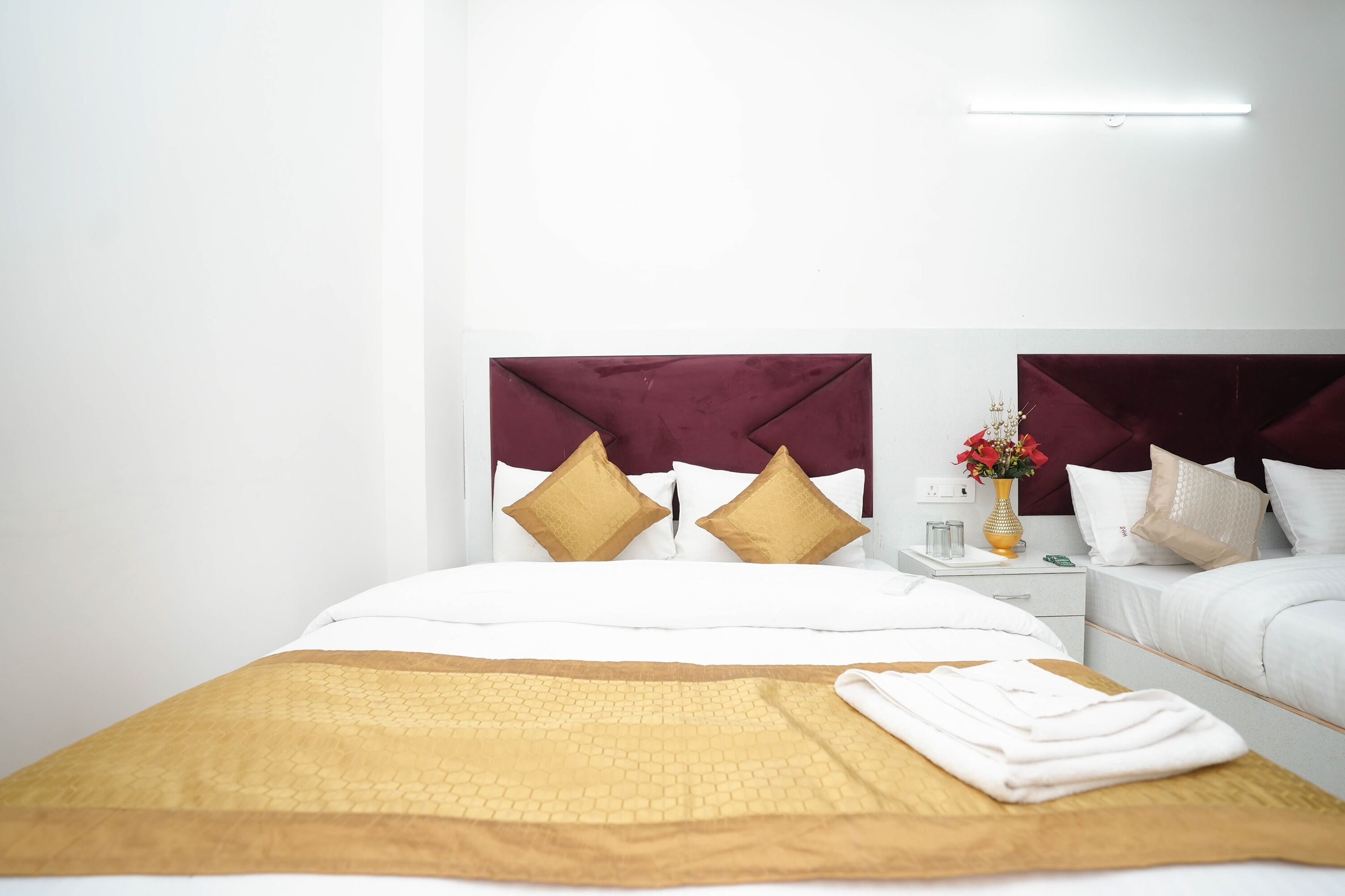 A hotel room with a large bed, two nightstands, a bedside table with a vase of flowers, and a modern headboard.