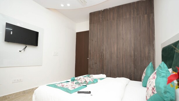 A modern bedroom with a large bed, a flat-screen TV mounted on the wall, and a wardrobe with a dark wood finish. - Sarthi Home Stay (New Delhi)