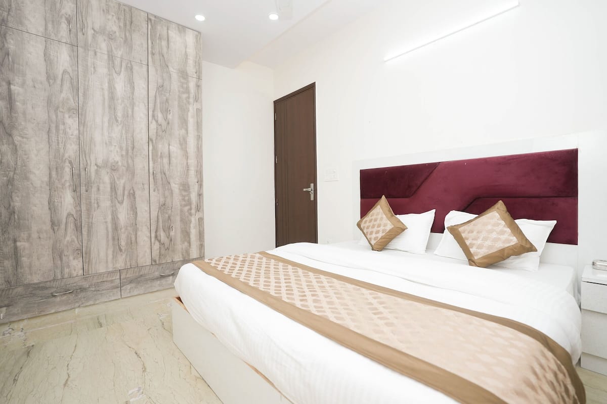 A modern hotel room with a large bed, a wooden wardrobe, and a marble floor.