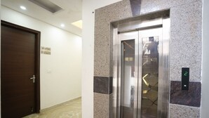 A reception area with a reception desk, a sign indicating no smoking, and an elevator with a digital display. - Sarthi Home Stay (New Delhi)