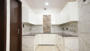 A narrow kitchen with white cabinets, a marble backsplash, and a sink. - Sarthi Home Stay (New Delhi)