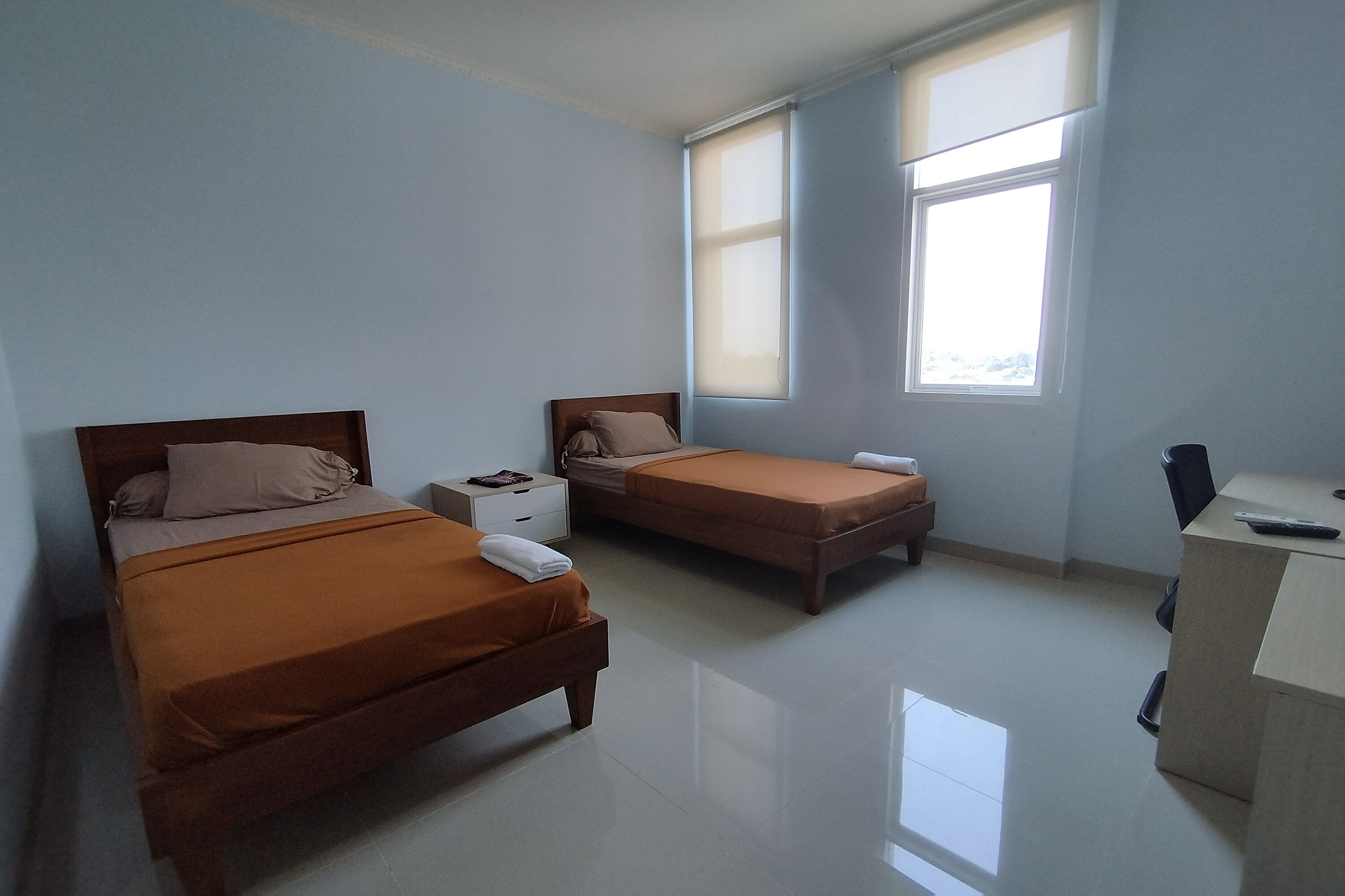 A bedroom with two beds, a desk, and a window.