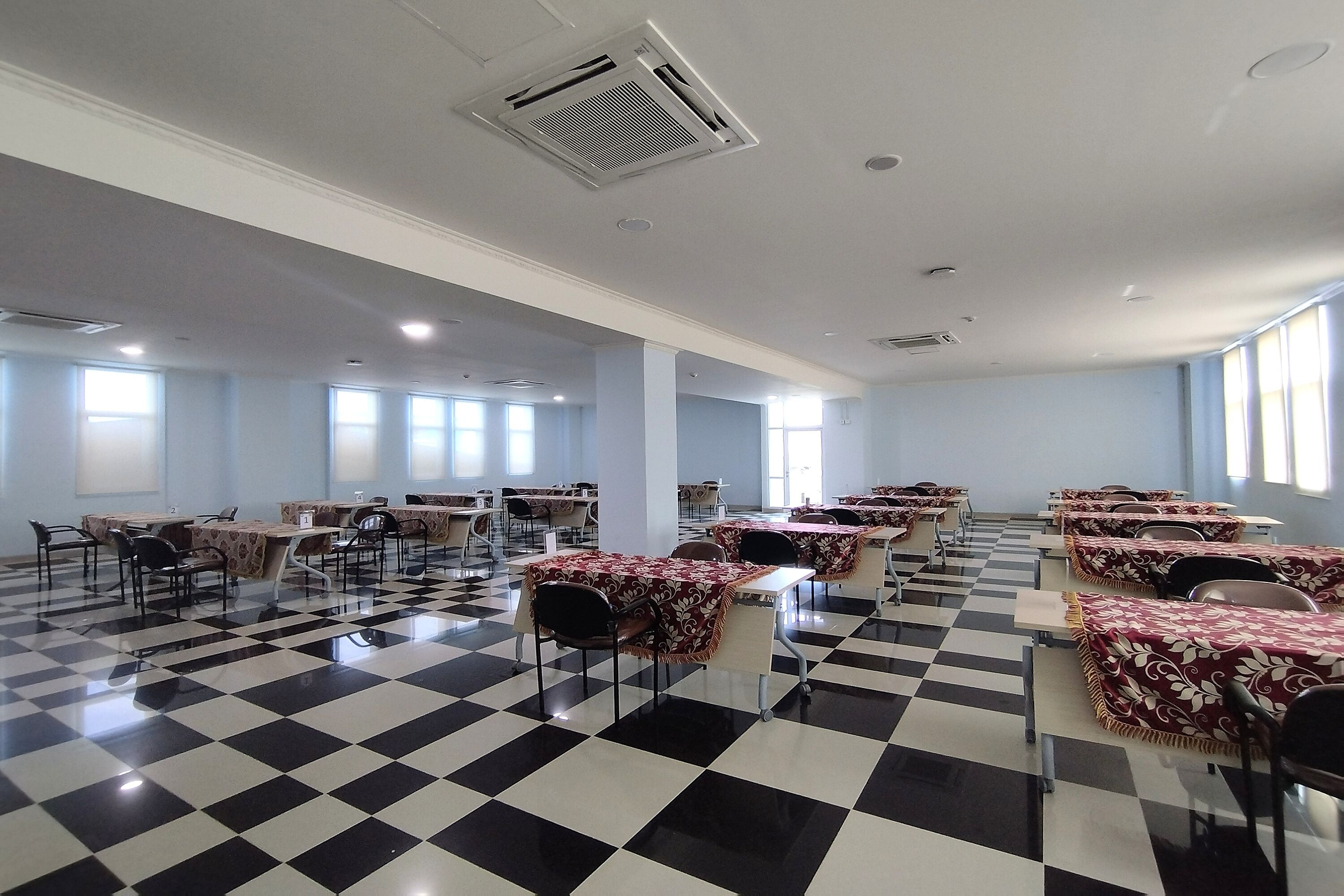 A dining area with checkered flooring, tables with floral tablecloths, and chairs.