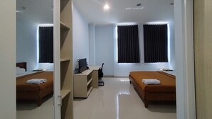 A hotel room with two beds, a desk with a computer, and a window with curtains. - Hotel Sutha Inn Syariah (Jambi)