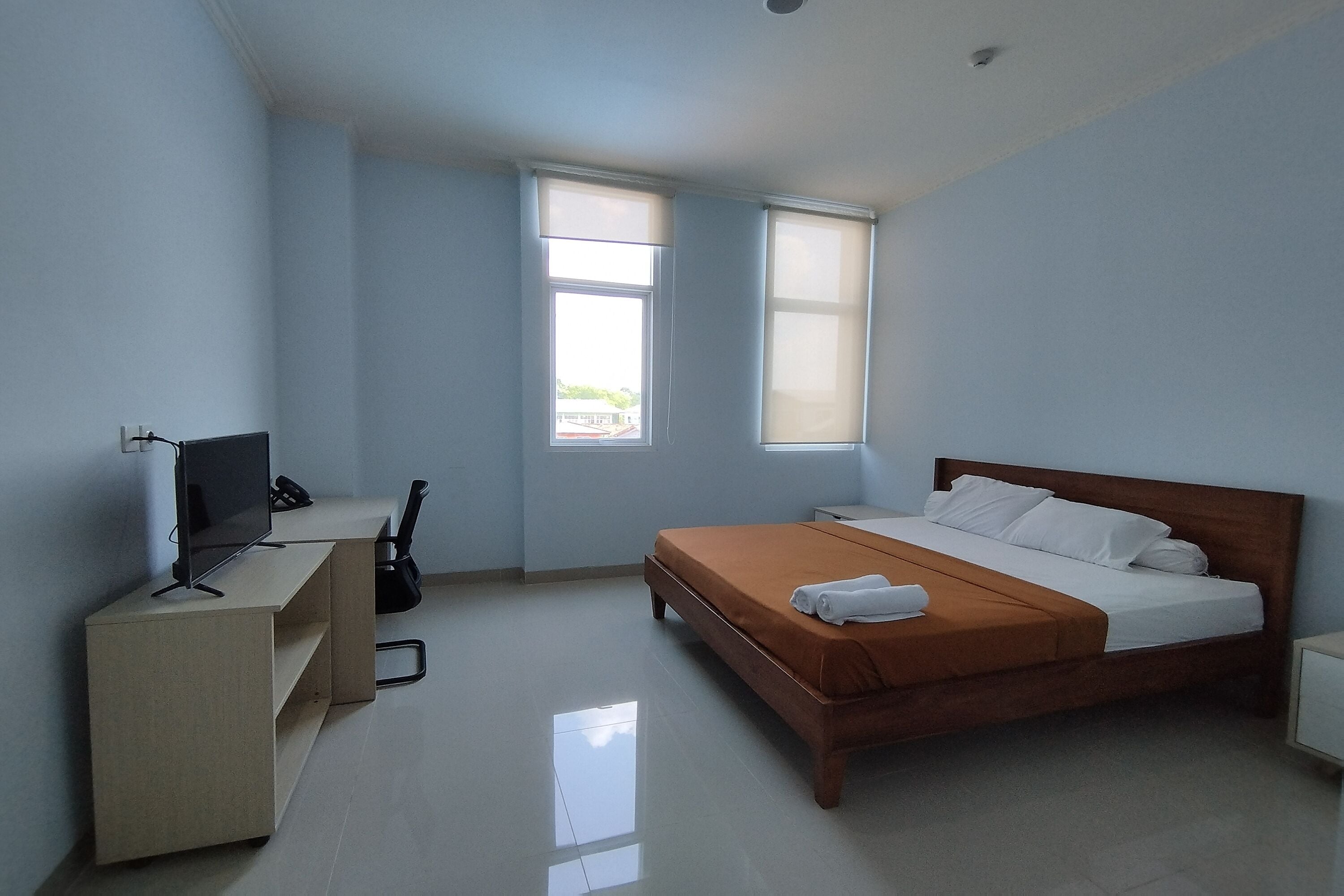 A bedroom with a bed, a desk, a chair, a television, and two windows.