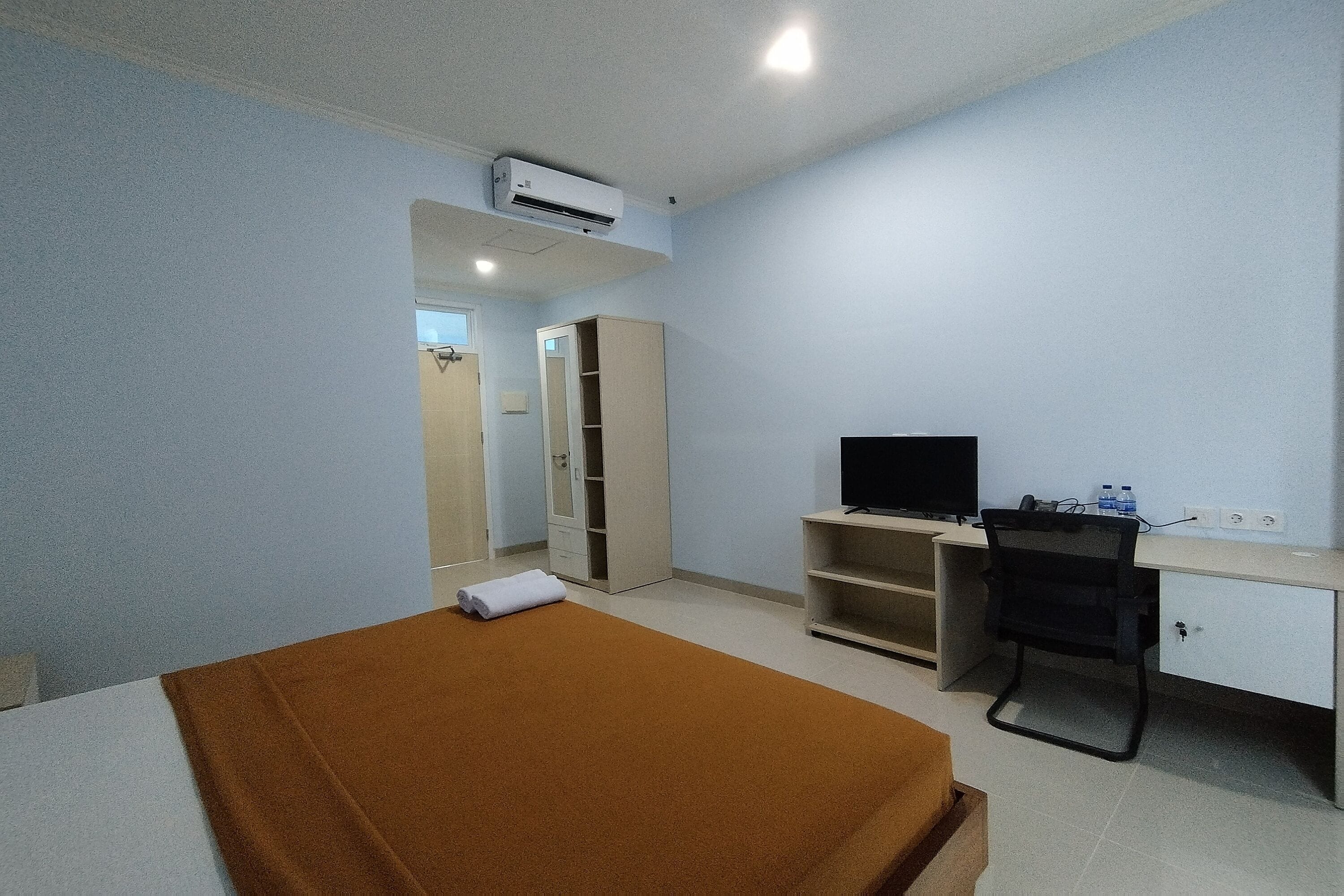 A hotel room with a bed, a desk, a chair, a TV, and a wardrobe.