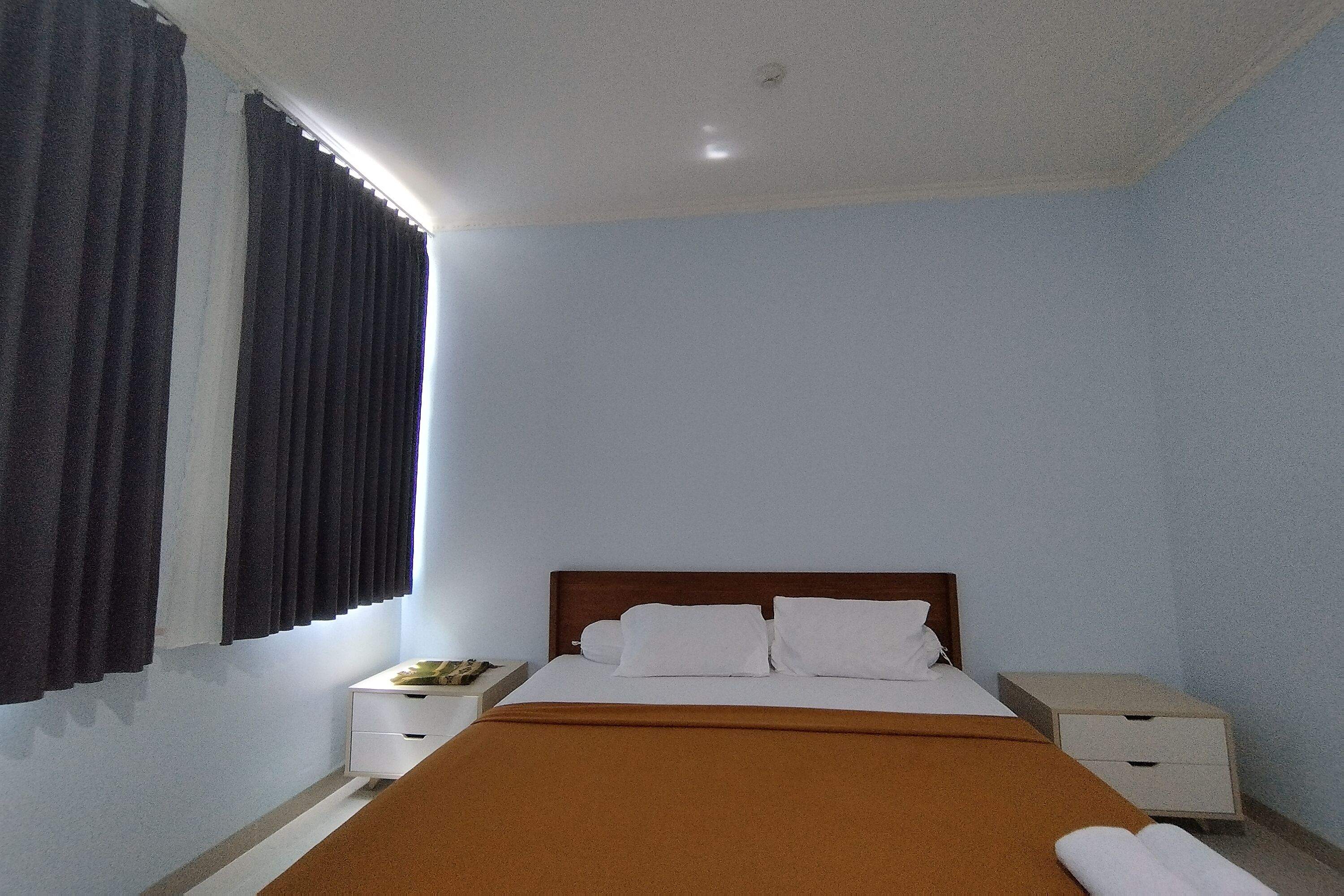 A bedroom with a single bed, white bedding, a brown throw blanket, and two bedside tables with lamps.