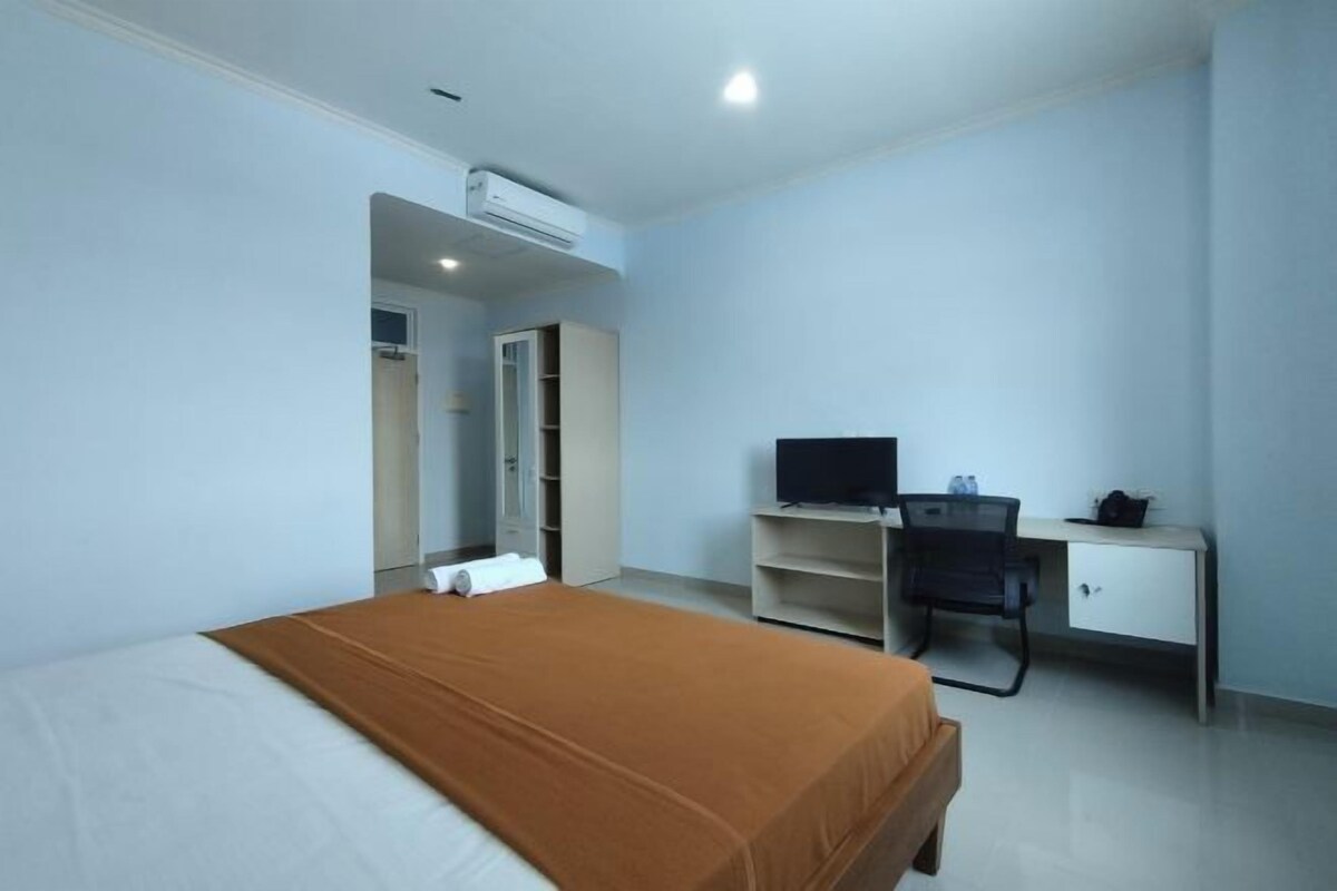 Una habitación de hotel con una cama, un escritorio con computadora y un armario.