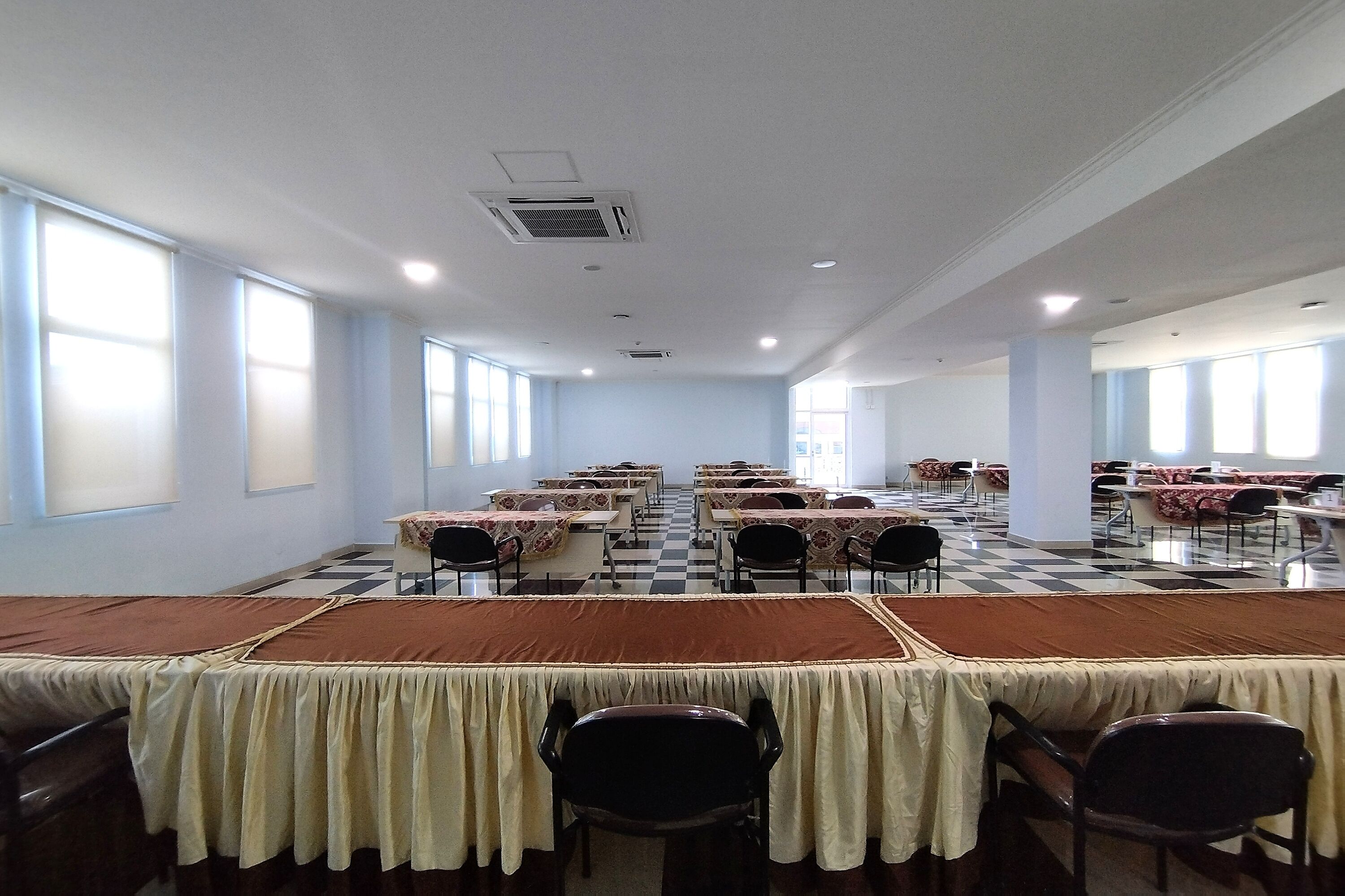 A large conference room with multiple tables and chairs, arranged in rows.