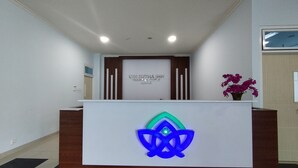 A reception desk with a logo, a sign above it, and a potted plant. - Hotel Sutha Inn Syariah (Jambi)