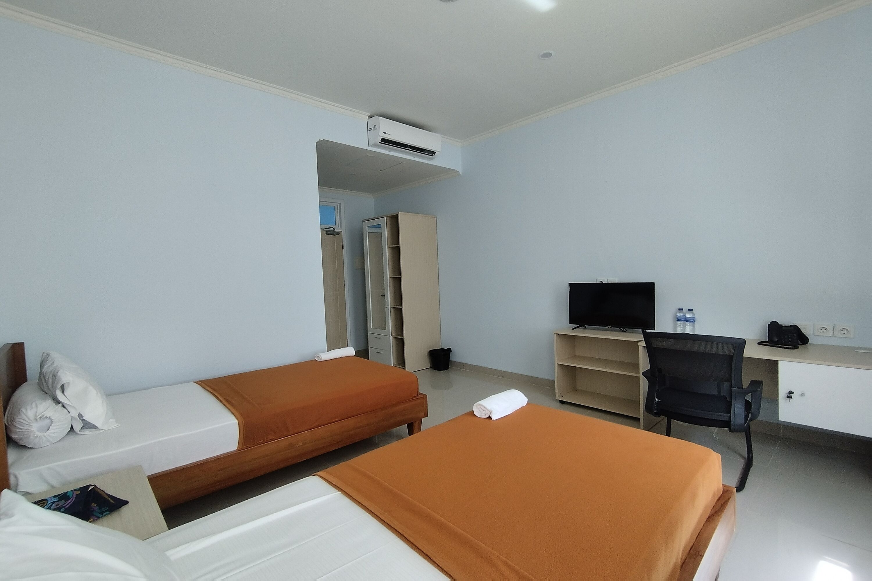A hotel room with two beds, a desk with a computer, a TV, and a wardrobe.