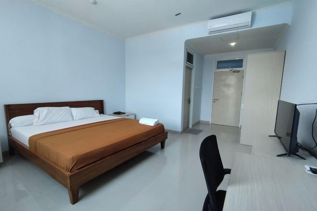 Una habitación de hotel con cama, escritorio, silla, televisor y aire acondicionado.
