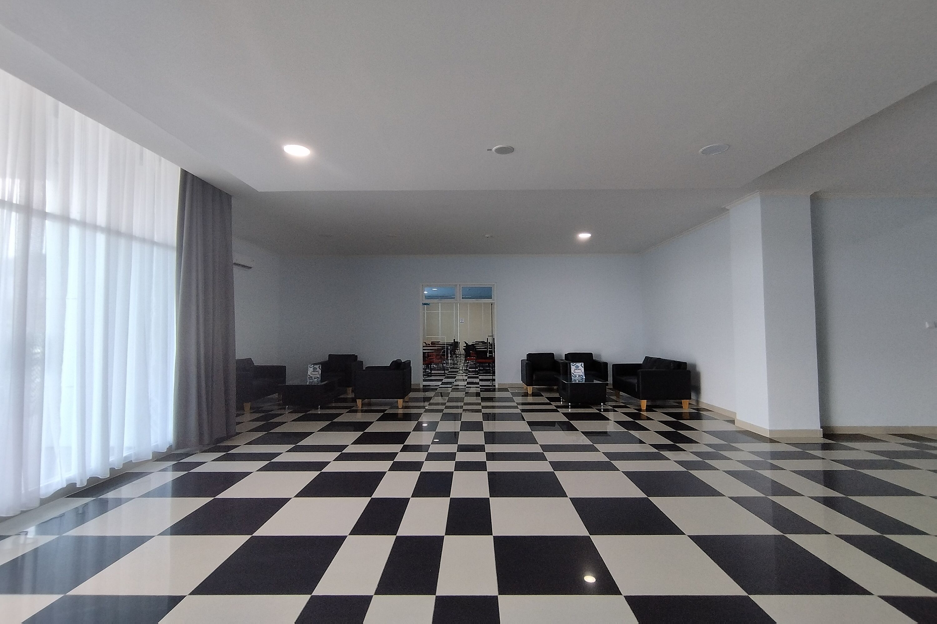 Un hall d’hôtel avec un sol à carreaux, un espace salon et de grandes fenêtres dotées de rideaux.